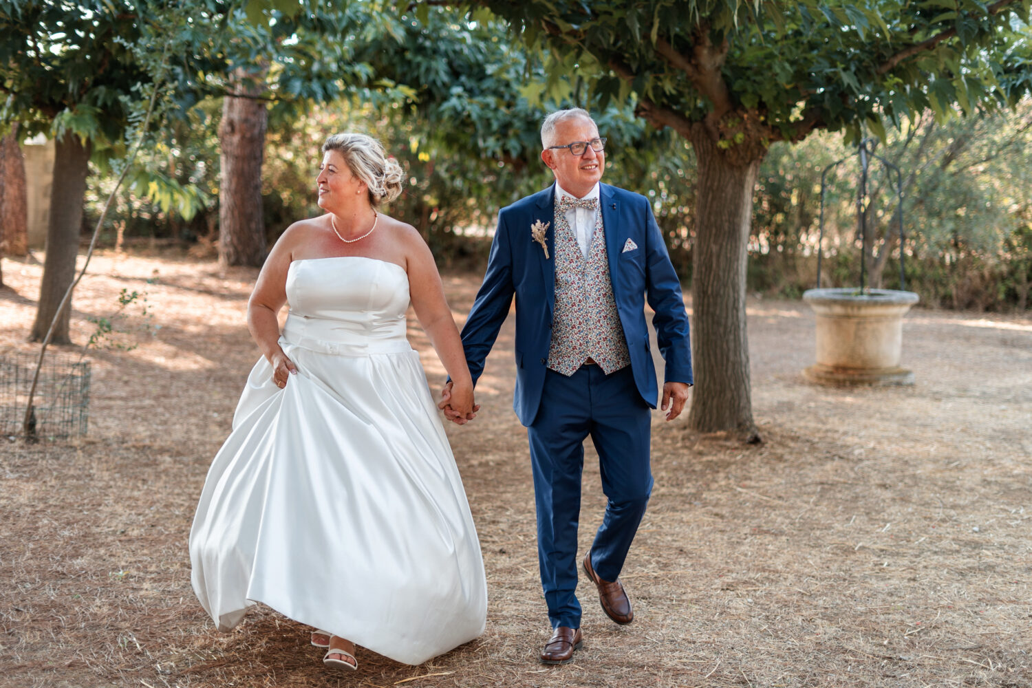 Des mariés se tiennent la main en marchant dans un domaine de Provence.